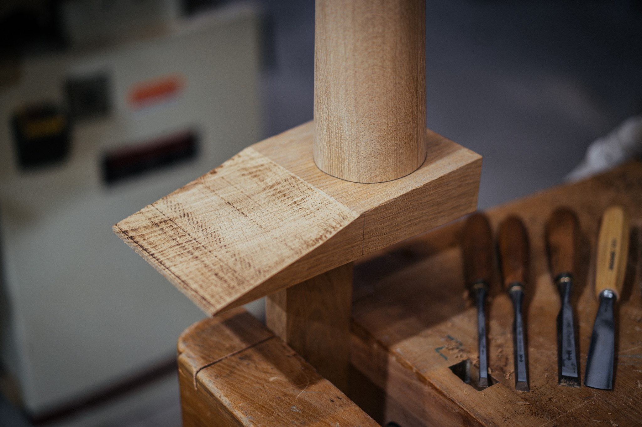 Passgenaue Holzverbindung an einem gedrechselten Tischbein, mit Stecheisen im Hintergrund